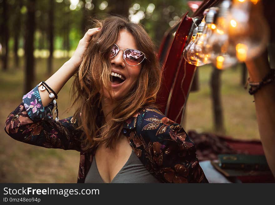 Image of amusing woman 20s wearing stylish accessories smiling while resting in forest camp. Image of amusing woman 20s wearing stylish accessories smiling while resting in forest camp