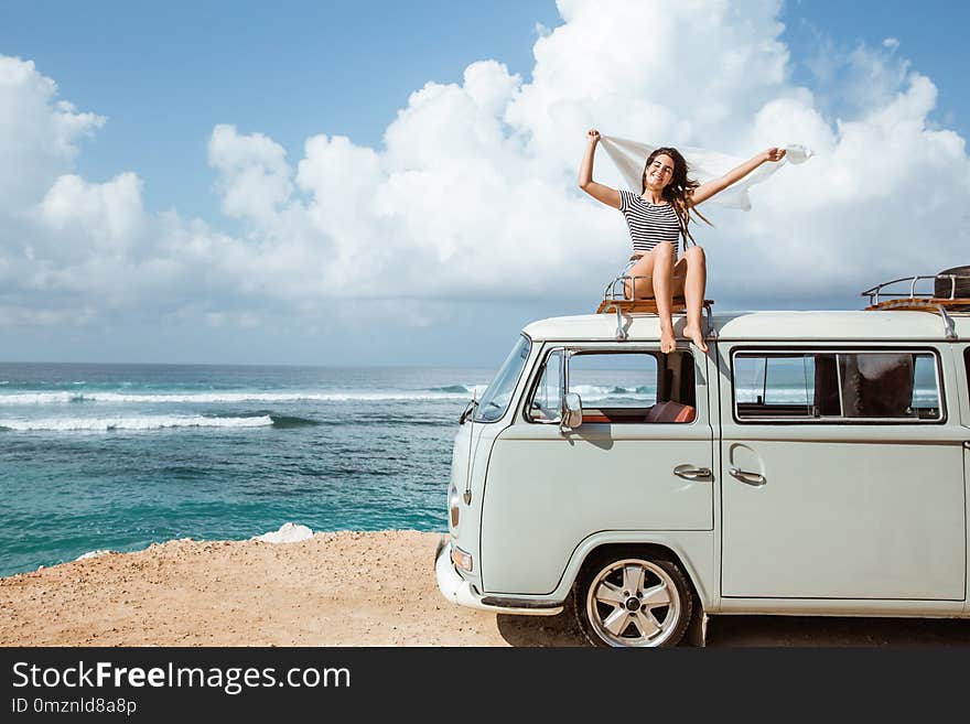 Beauty woman enjoy blow wind with waving white scarf on the retro van roof at the beach