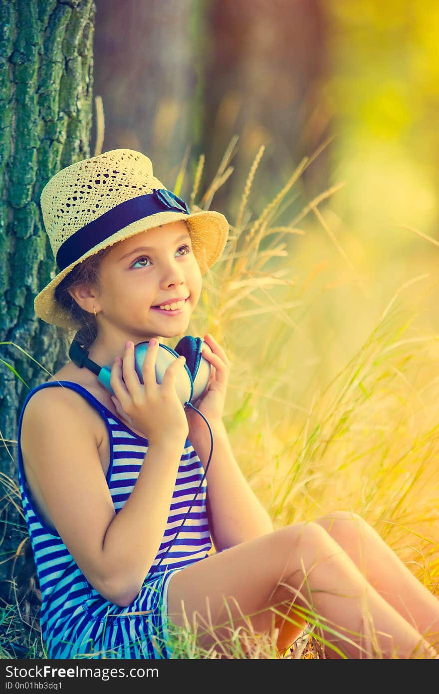 Portrait of the beautiful girl with earphones sitting near the tree