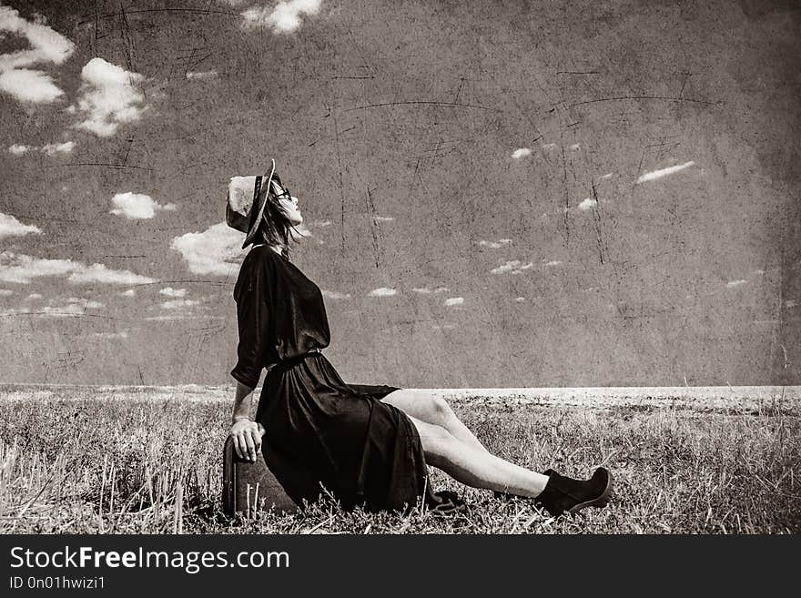 Photo of the beautiful young woman sitting on the suitcase in the field . Image in black and white color style. Photo of the beautiful young woman sitting on the suitcase in the field . Image in black and white color style