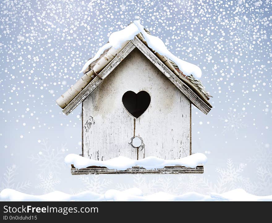 White wooden bird house winter snow falling down on bark roof heart shape