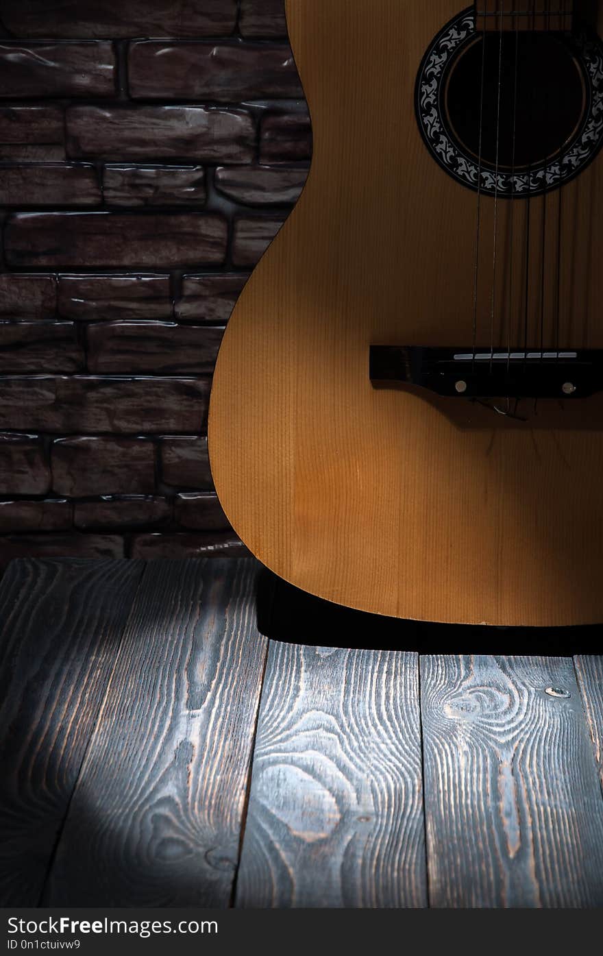 A beam of light in front of an acoustic guitar standing by a brick wall on wooden boards.