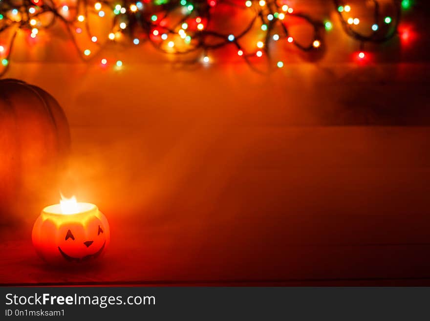 Halloween candle in the dark on a wooden background. Behind the pumpkin in the lights of the garland.