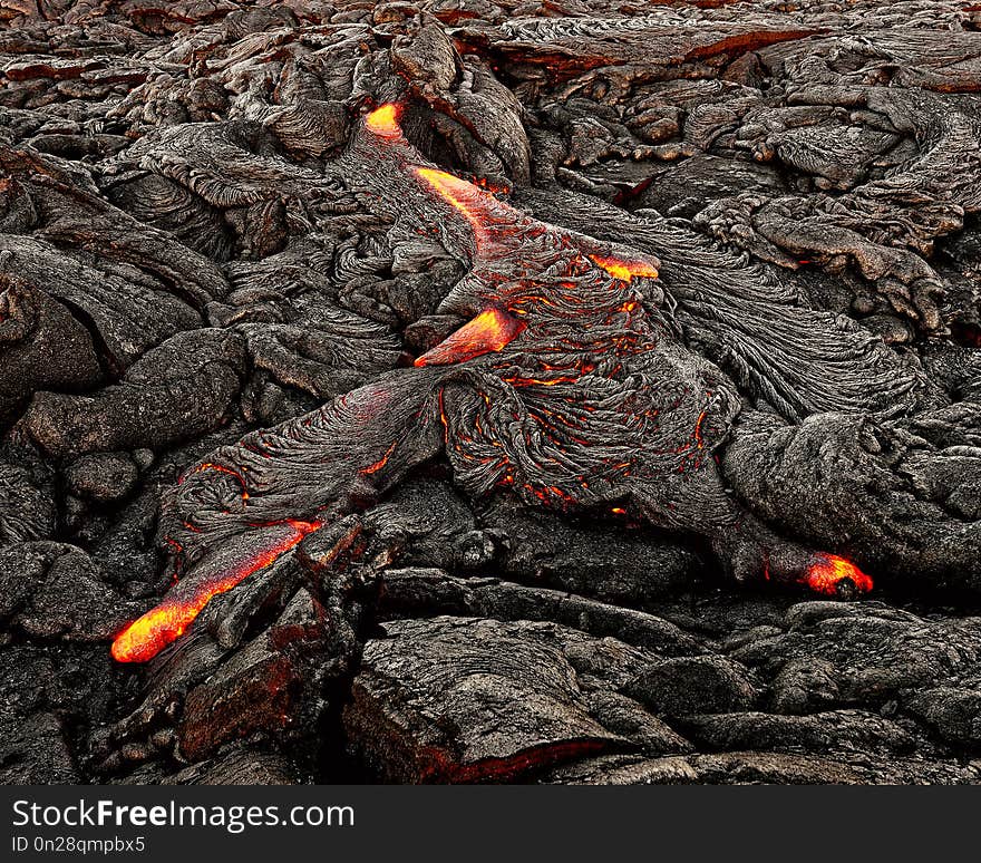 A lava flow emerges from an earth crevice and flows in a black volcanic landscape, glowing magma, first daylight - Location: Hawaii, Big Island, volcano `Kilauea `. A lava flow emerges from an earth crevice and flows in a black volcanic landscape, glowing magma, first daylight - Location: Hawaii, Big Island, volcano `Kilauea `