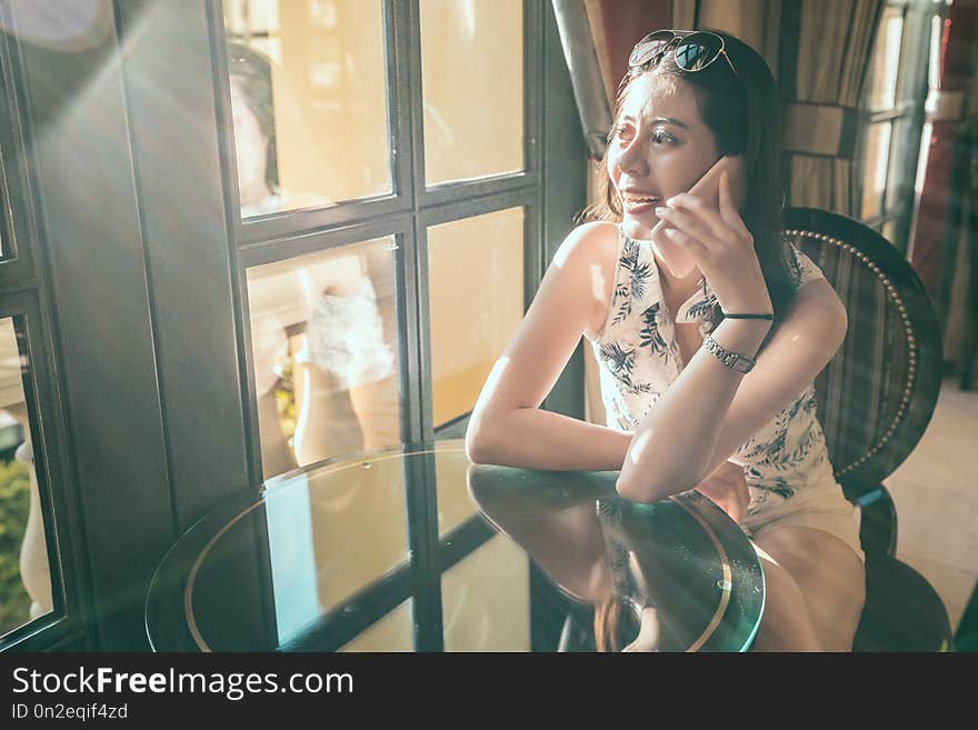 Beautiful traveler on mobile phone chatting with friends. lady sitting at home near the ceiling window in a classic design room. Enjoying sunlight flare in the house. Beautiful traveler on mobile phone chatting with friends. lady sitting at home near the ceiling window in a classic design room. Enjoying sunlight flare in the house.