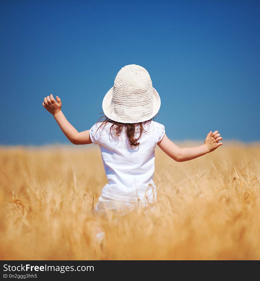 Happy girl walking in golden wheat, enjoying the life in the field. Nature beauty, blue sky and field of wheat. Family outdoor lifestyle. Freedom concept. Cute little girl in summer field