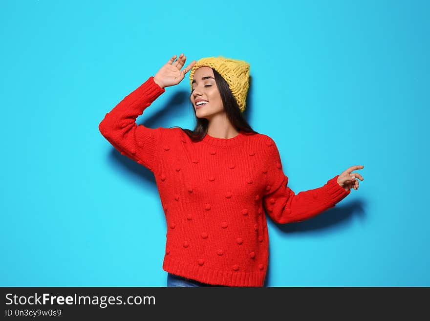 Young woman in warm sweater and hat on color background. Celebrating Christmas