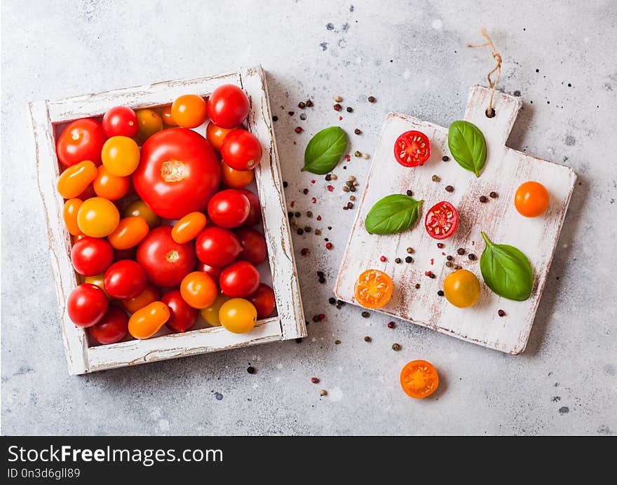 Organic Tomatoes with basil in vintage wooden box on stone kitchen table background. San Marzano, orange and plum tomatoes