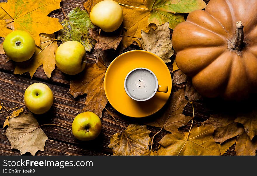 Photo of the fallen leaves, pumpkin, apples and yellow cup of coffee on the brown wooden background. Photo of the fallen leaves, pumpkin, apples and yellow cup of coffee on the brown wooden background