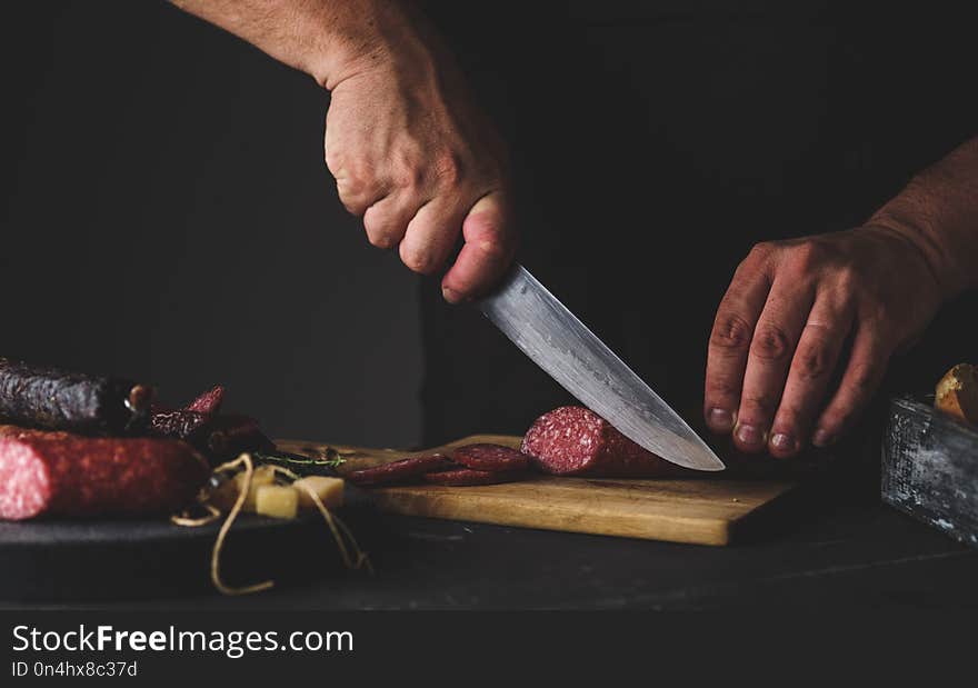 Men`s hands cut sausage salami on a cutting board.