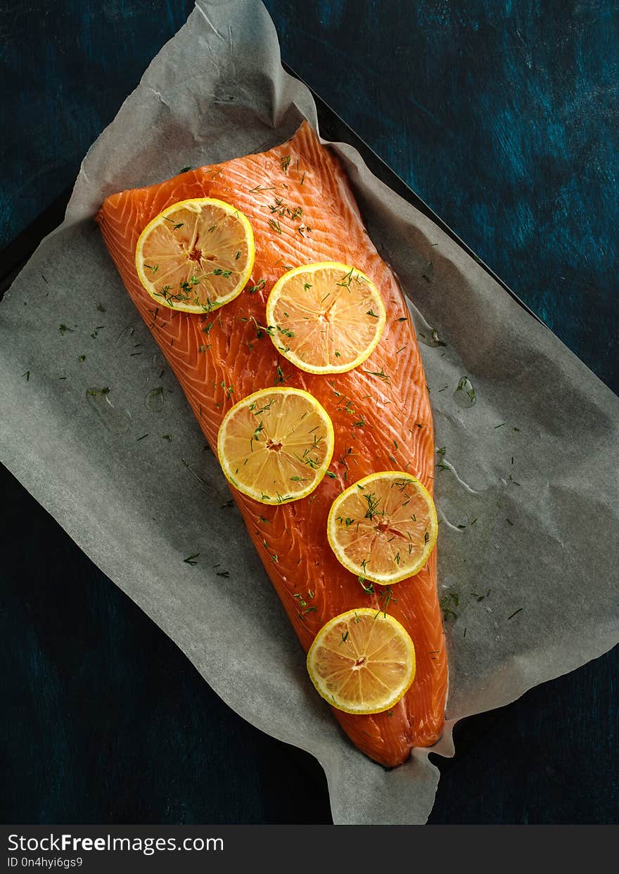 Raw fillet of salmon with lemons on a baking sheet.