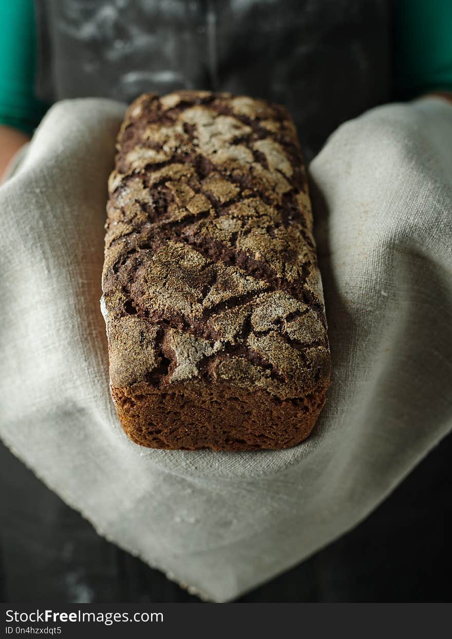 Female hands hold rye bread on dark background.