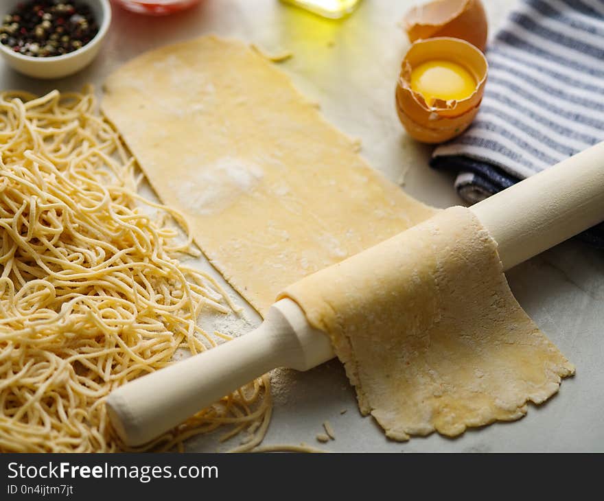 Homemade pasta dough is being processed. Rolled dough for homemade italian uncooked pasta over white marble texture background. Homemade pasta dough is being processed. Rolled dough for homemade italian uncooked pasta over white marble texture background.