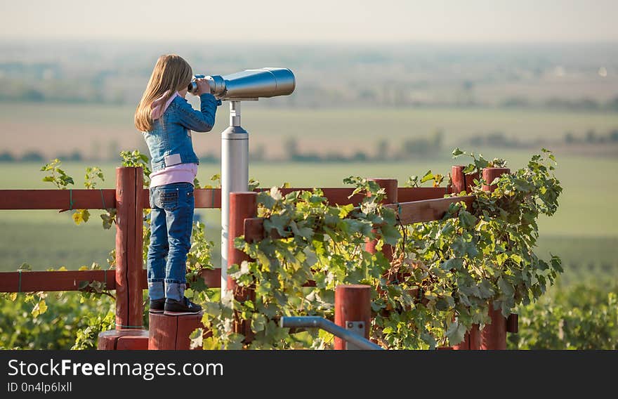 Little blond girl standing on the sp in the wooden fance of the Moravian field and looking into spyglass. Little blond girl standing on the sp in the wooden fance of the Moravian field and looking into spyglass