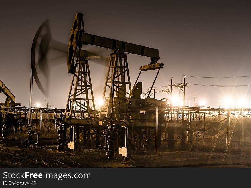 Working oil pump jack at night time. Oilfield during winter. Refinery lights background. Oil and gas concept. Toned.