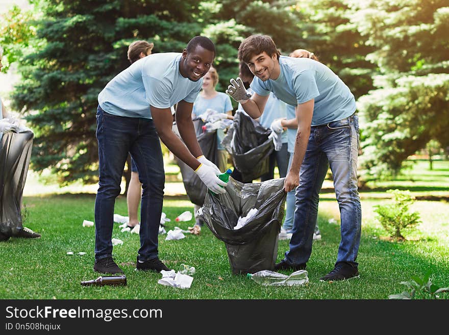 Multiethnic young men volunteers cleaning park, caring about environment, copy space. Multiethnic young men volunteers cleaning park, caring about environment, copy space