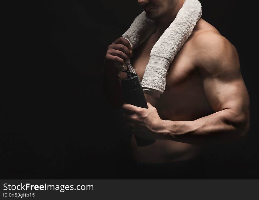 Athletic young man having rest after bobybuilding training, drinking water on a black background. Naked torso, muscular body. Strong chest and shoulder muscles. Studio shot, low key, copy space. Athletic young man having rest after bobybuilding training, drinking water on a black background. Naked torso, muscular body. Strong chest and shoulder muscles. Studio shot, low key, copy space