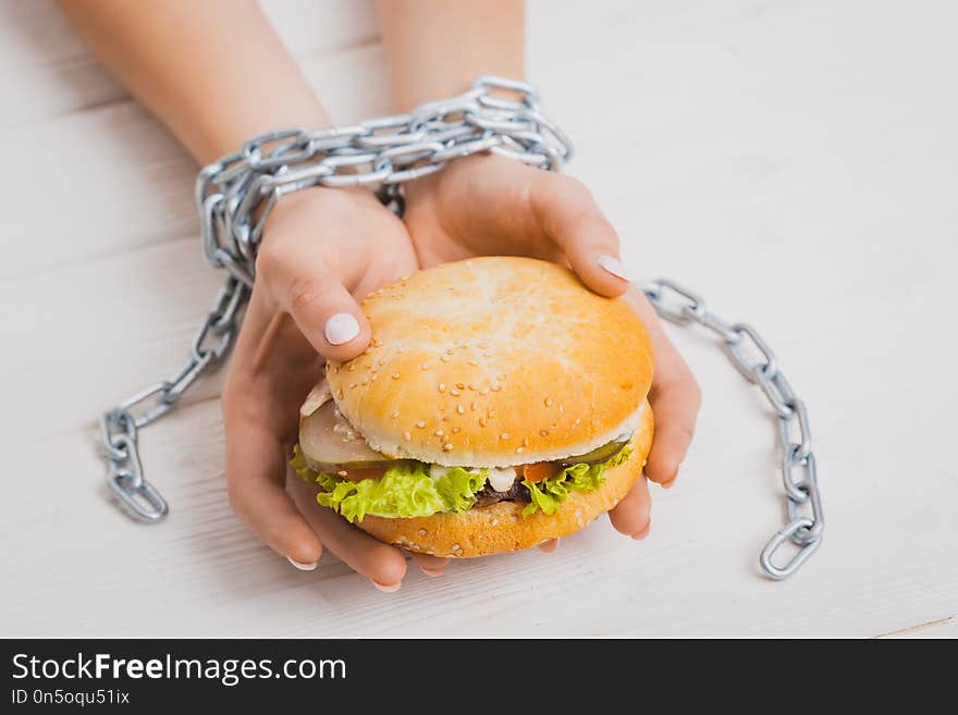 Steel chain-bound female hands with burger. Concept weight loss, junk food