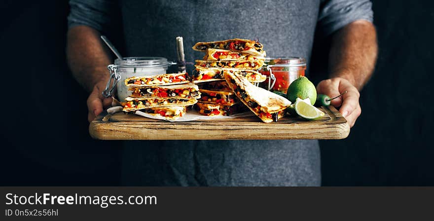 In the hands man cutting board with vegetarian snacks: quesadilla with vegetables and cheese on dark background. In the hands man cutting board with vegetarian snacks: quesadilla with vegetables and cheese on dark background