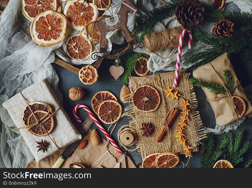 Christmas or New Year composition with handmade gifts, dry oranges, cinnamon, fir tree on dark stone table. Holidays preparations