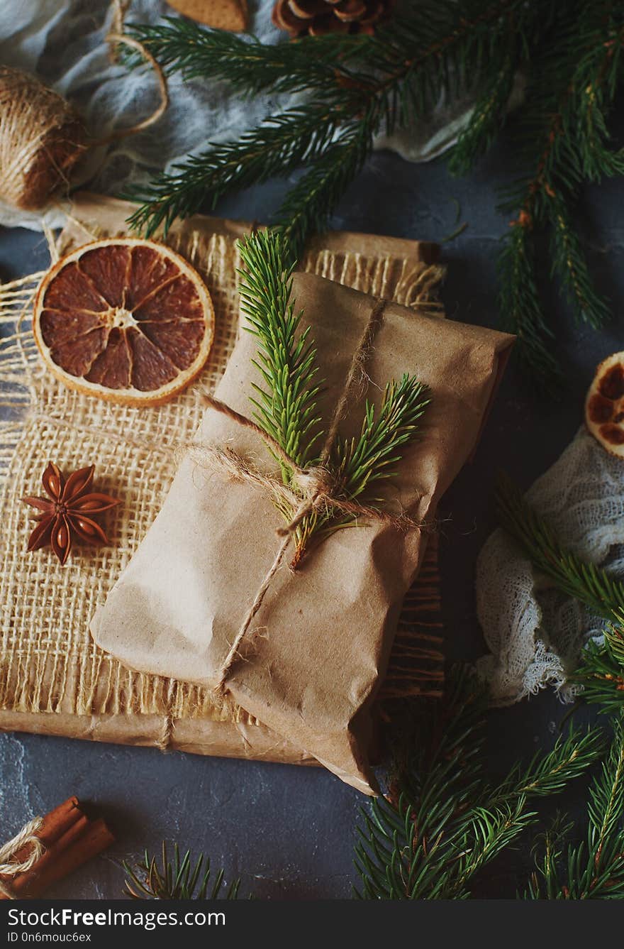 Christmas or New Year composition with handmade gifts, dry oranges, cinnamon, fir tree on dark stone table. Holidays preparations