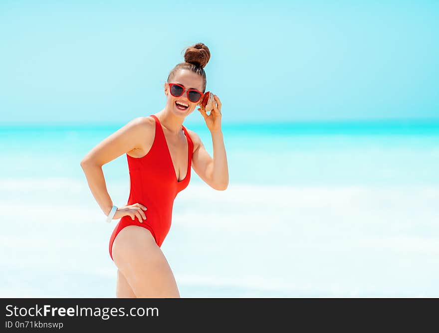 Smiling woman on seacoast listening to sound of ocean in shell