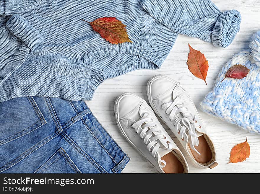 Stylish outfit and autumn leaves on white wooden background, flat lay. Trendy warm clothes