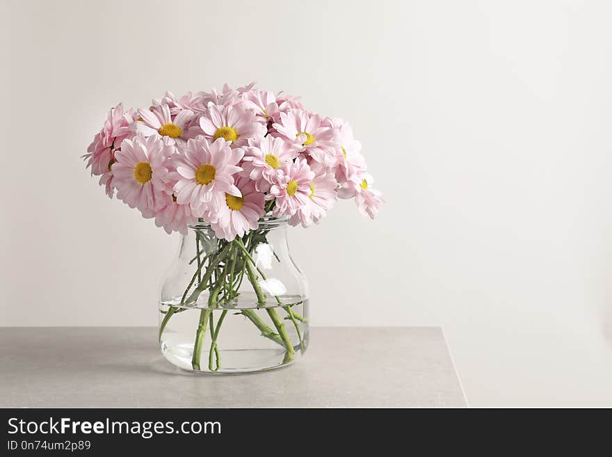 Vase with beautiful chamomile flowers on table against light background. Space for text