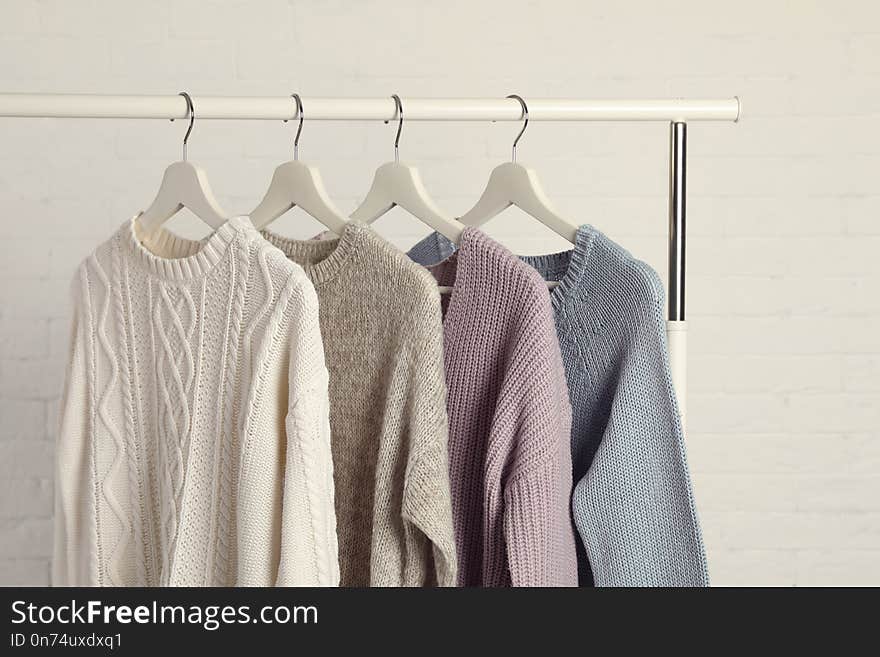 Collection of warm sweaters hanging on rack against white brick wall