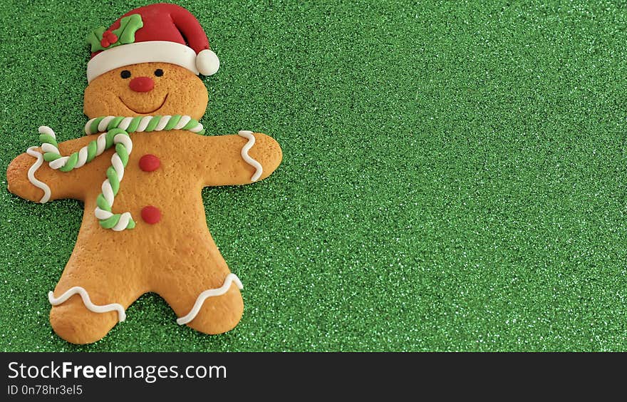 Gingerbread man cookie laying flat on a festive green background with copy space. it is decorated with a red Santa hat with holly leaves and he has a green and white scarf around neck with red buttons on body. Gingerbread man cookie laying flat on a festive green background with copy space. it is decorated with a red Santa hat with holly leaves and he has a green and white scarf around neck with red buttons on body