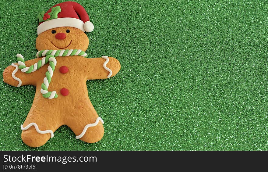 Gingerbread man with red Santa hat green and white scarf on a green background with writing space