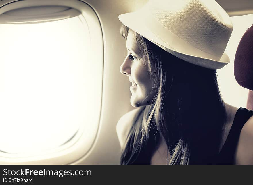 Young woman is looking through a window in the atplane. Pastel colors. Great vacation and travel concept. Young woman is looking through a window in the atplane. Pastel colors. Great vacation and travel concept