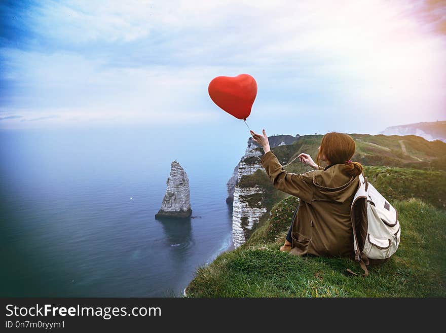 Happy girl with a red balloon in the shape of a heart at background of scenery Etretat. France. Happy girl with a red balloon in the shape of a heart at background of scenery Etretat. France