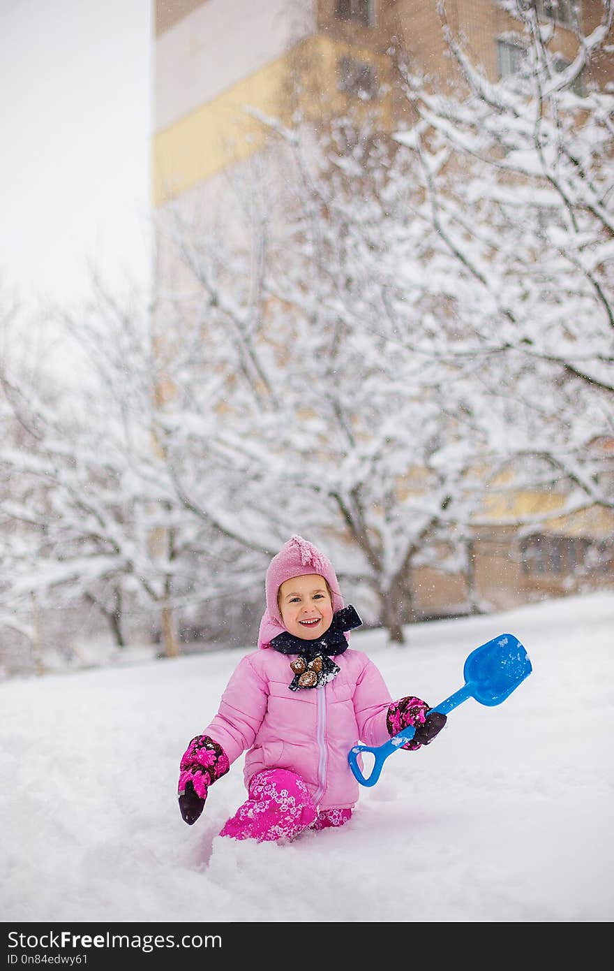 The child plays with snow in the winter. A little girl in a bright jacket and knitted hat, catches snowflakes in a winter park for Christmas. Children play and jump in the snow-covered garden.