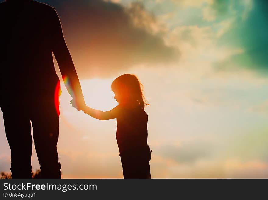 Silhouette of little girl holding parent hand at sunset