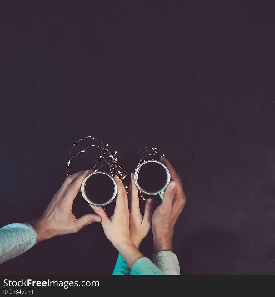 Couple in love holding hands with coffee on black table, with christmas lights. Photograph taken from above, top view