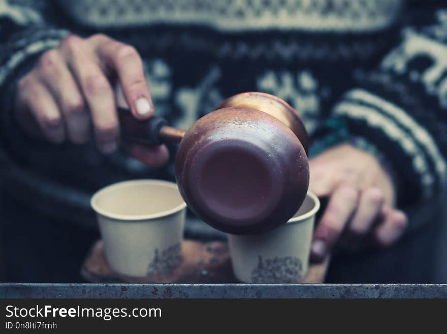 Street coffee cooking and pouring in paper cups. Closeup hands photo with selective focus on coffee pot.