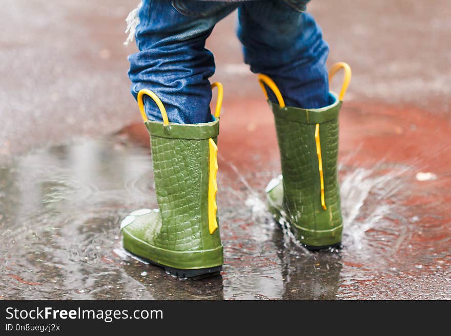 Child with rain boots jumps into a puddle with leaf, autumn concept