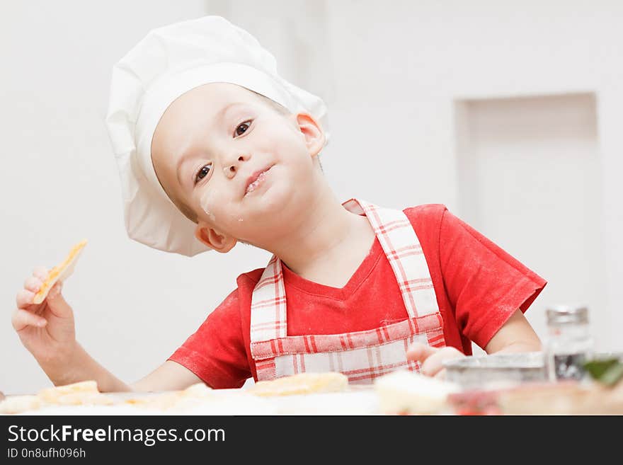 Little cheerful boy chef cooks and eats homemade pizza. Little cheerful boy chef cooks and eats homemade pizza