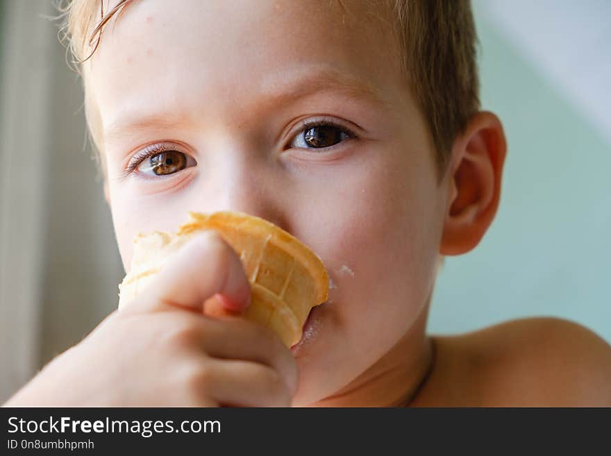 Small boy with charming eyes is holding and eating ice-cream