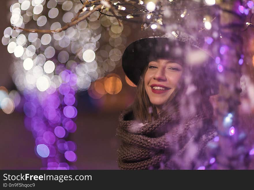 Young girl standing in front of christmas tree lights at night w