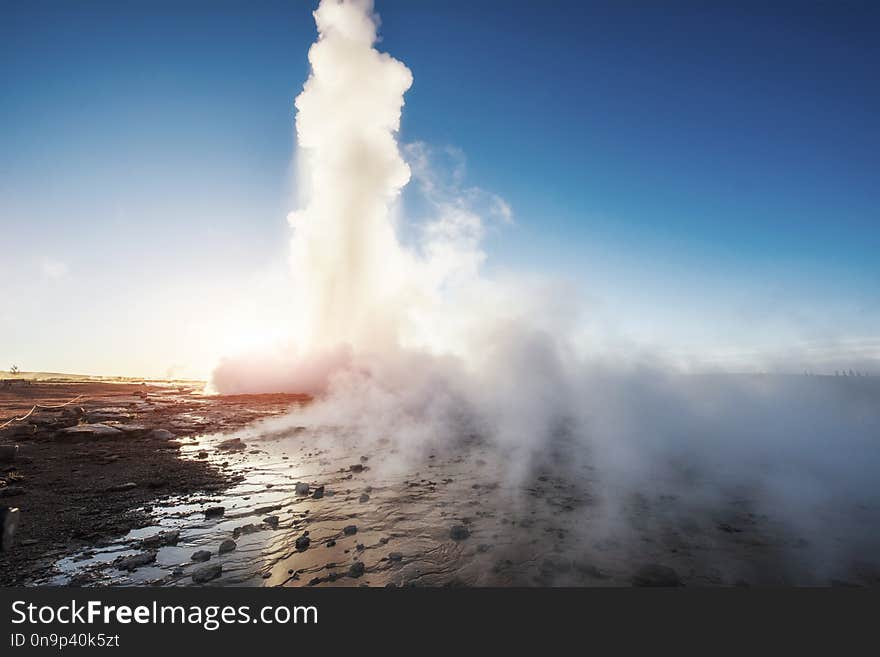 Strokkur Geyser Eruption In Iceland. Fantastic Colors Shine Through The Steam. Beautiful Pink Clouds In A Blue Sky