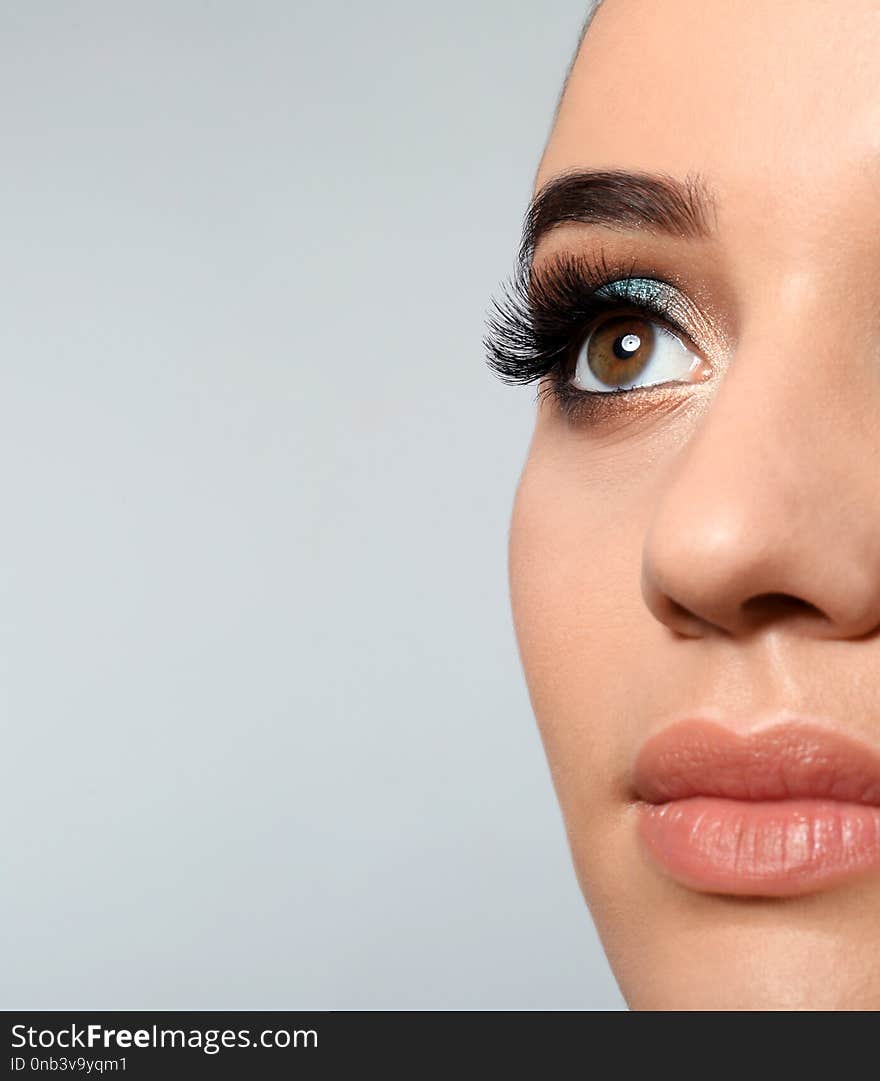 Young woman with eyelash extensions and beautiful makeup on light background.