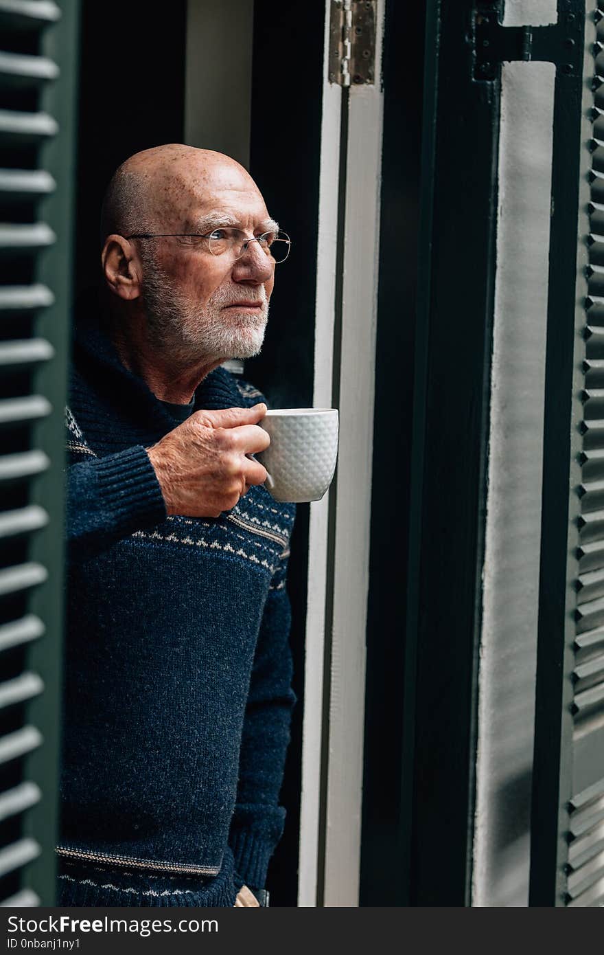 Senior person standing near the door drinking coffee. Old person drinking coffee while looking out of the door.