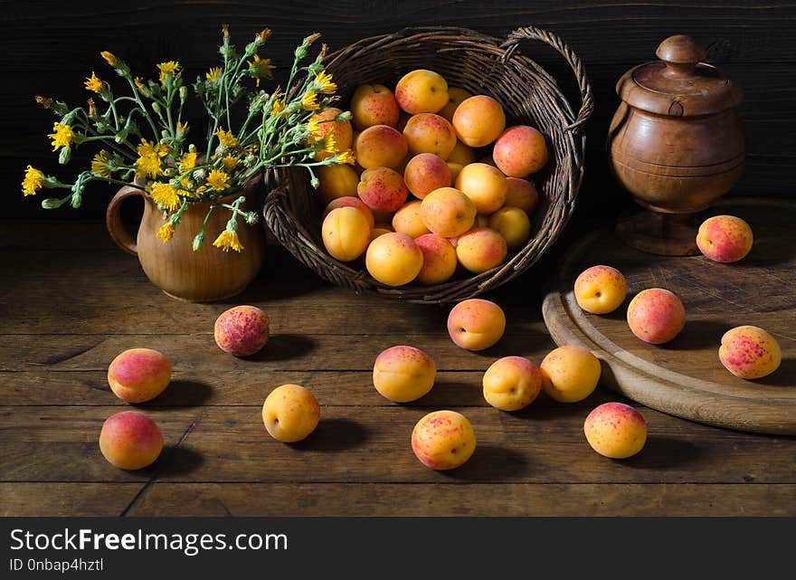 Apricots in a basket and a bouquet of yellow flowers on a wooden table. Dark photo, rustic style. Apricots in a basket and a bouquet of yellow flowers on a wooden table. Dark photo, rustic style