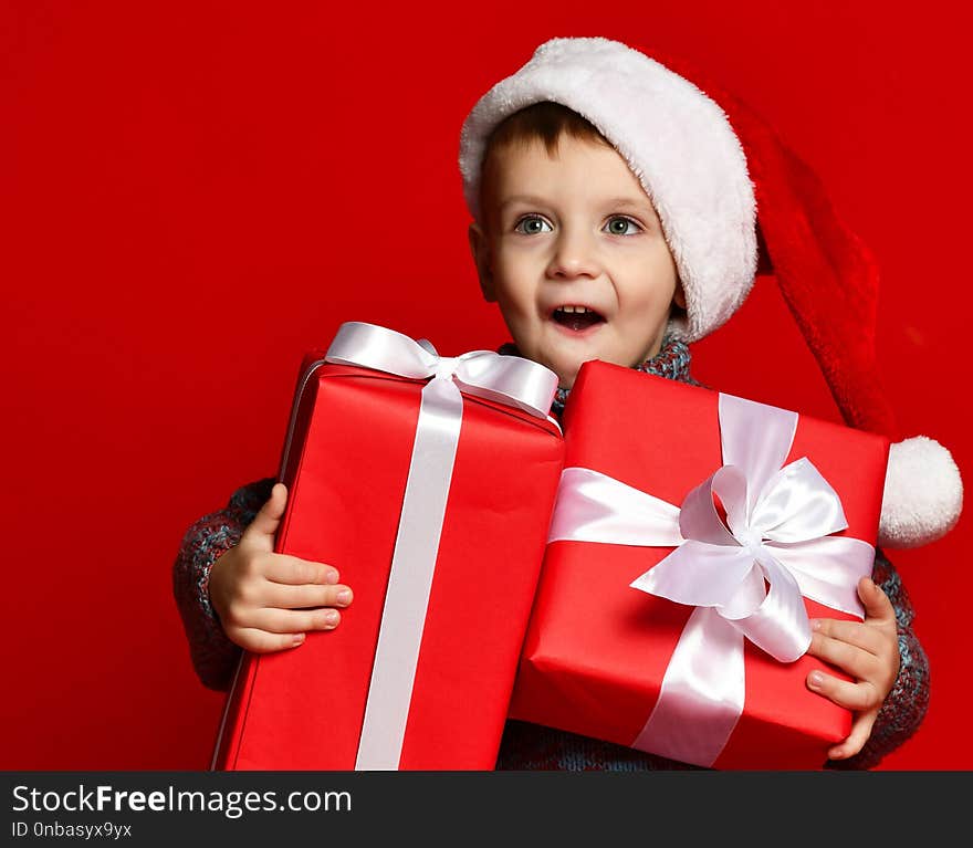 Funny smiling child in Santa red hat holding Christmas gift in hand.