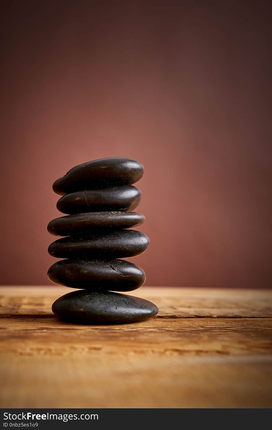 Stack of black spa stones for massage on a brown background and an old wooden table
