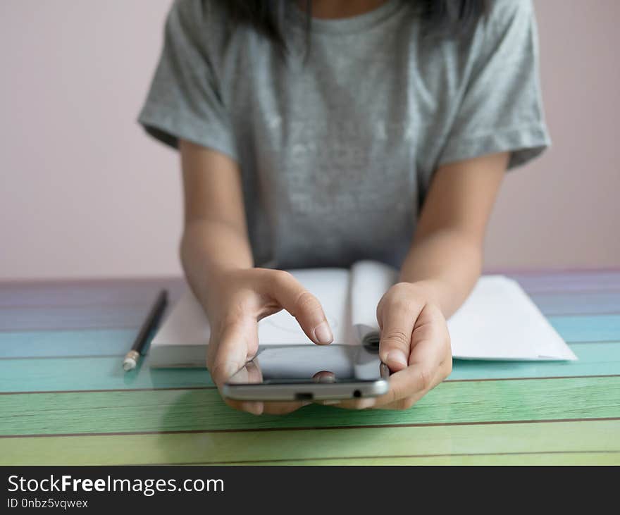 A little girl playing smartphone with doing homework on the colourful table