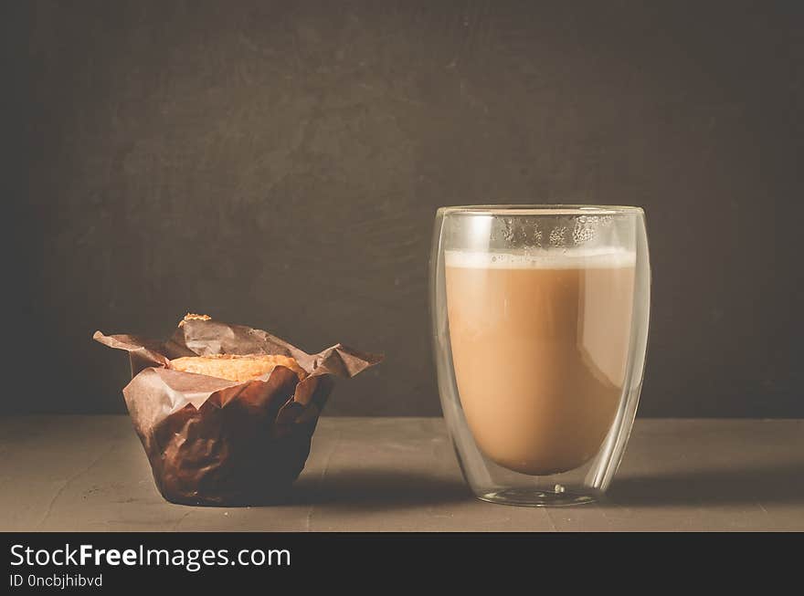 Cake with a chocolate stuffing in paper and a cappuccino cup/cake with a chocolate stuffing in paper and a cappuccino cup on a dark background. Selective focus