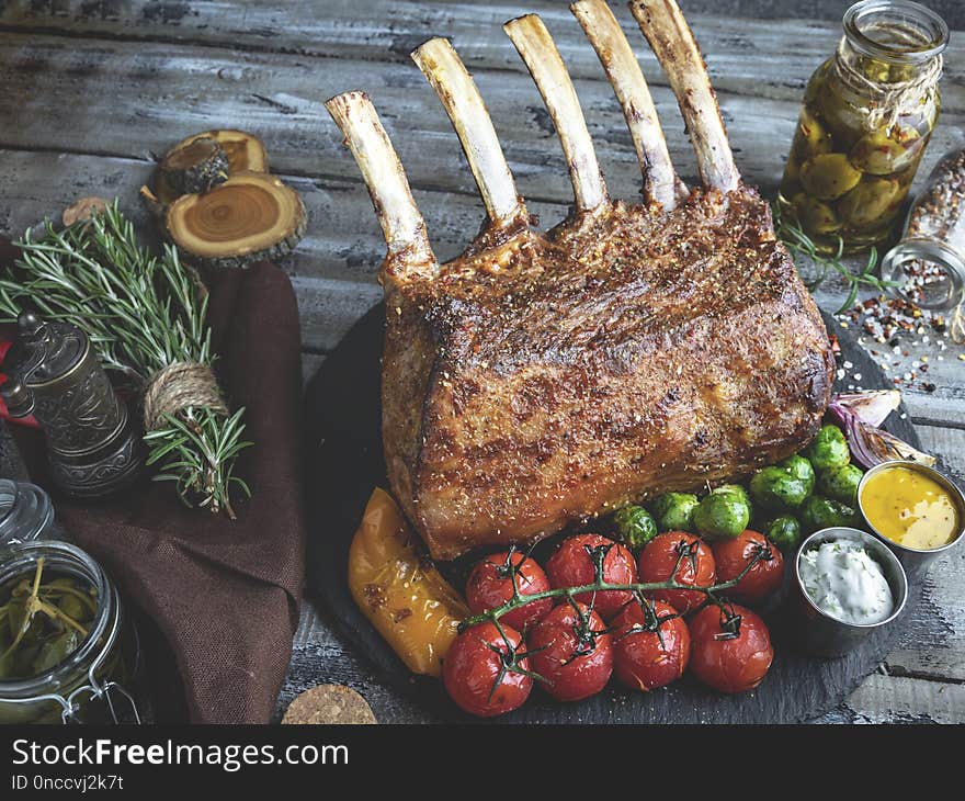 Grilled roasted rack of lamb chops with vegetables, on a wooden surface.